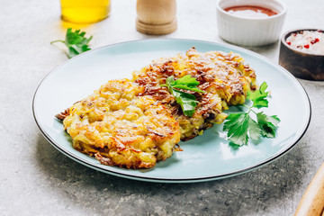 Homemade potato pancakes or hash brown on blue plate with sauce on gray table. Traditional dish in European and American cuisine. Selective focus.