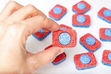 Hands holding many red and blue dishwasher soap tablets close up, white background