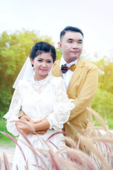 Portrait Valentine Day Concept. Wedding love moment in natural park garden. Asian Thai couple of newlyweds. Woman bride smiling groom man. Model looking camera and sunset light blurred background.