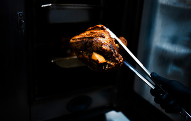 juicy grilled meat piece is kept in forceps with hands on a dark background