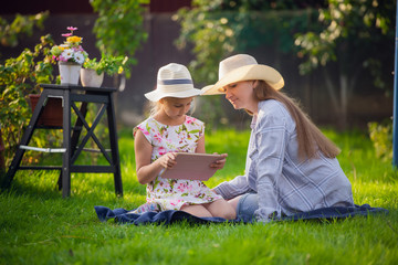 Happy loving family. Young mother and her daughter girl play outdoors. Funny mom and lovely child are having fun with tablet.