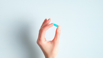 Female hand holding medical pill capsule over blue background. Pharmacy and medicine concept