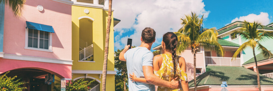 Couple on winter vacation taking pictures of pastel colored beach houses cottages in tropical holiday destination Fort Myers, Florida. Man tourist taking picture with phone.