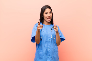 young latin nurse smiling with a positive, successful, happy attitude pointing to the camera,...