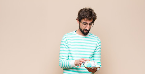 young man with macaroons against flat wall