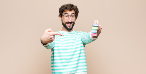 young man with macaroons against flat wall