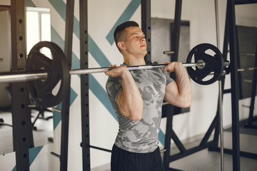 Fototapeta na wymiar Sports man in the gym. A man performs exercises. Guy in a gray t-shirt