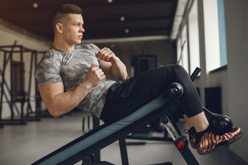 Fototapeta na wymiar Sports man in the gym. A man performs exercises. Guy in a gray t-shirt