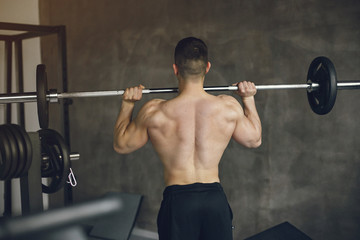 Fototapeta na wymiar Sports man in the gym. A man performs exercises. Guy in a black shorts.