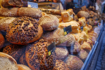 View of front store's display with heap and stack of wheat and rye breads with whole grain meal and rustic mustard crust at the front of bakery store on sidewalk in old town Düsseldorf, Germany. 