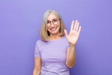 senior or middle age pretty woman smiling happily and cheerfully, waving hand, welcoming and greeting you, or saying goodbye