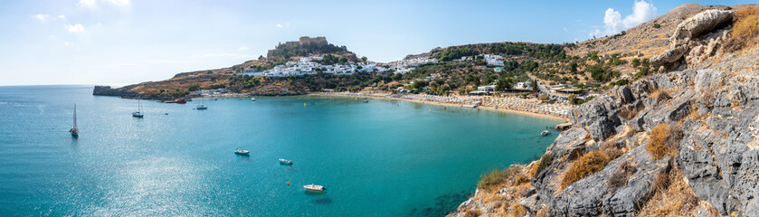 Naklejka na ściany i meble Lindos bay with famous beach and village of Lindos and Acropolis in background – panoramic (Rhodes, Greece)