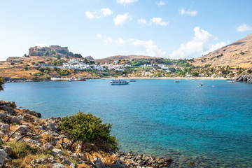 Obraz premium Lindos bay with boats, white houses of village of Lindos and Acropolis in background (Rhodes, Greece)