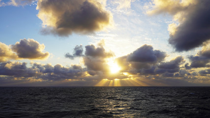 blue sky in the clouds. sunset sky, yellow white rays of the sun shine through the clouds on the ocean. sunset on the open sea, paradise. glow from heaven. cloudy sky
