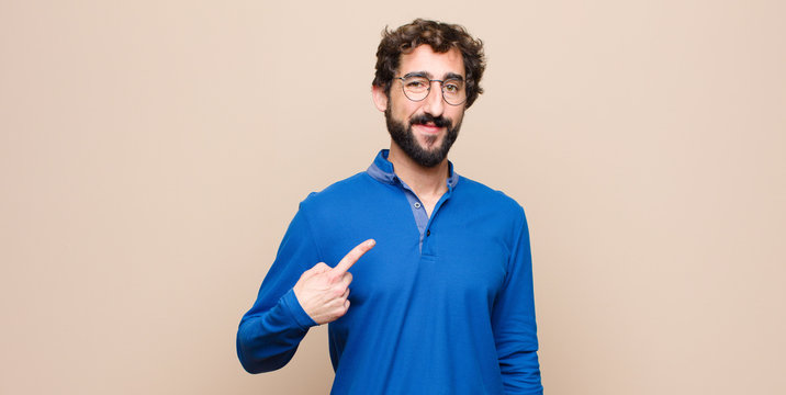 young handsome man looking proud, confident and happy, smiling and pointing to self or making number one sign against flat wall