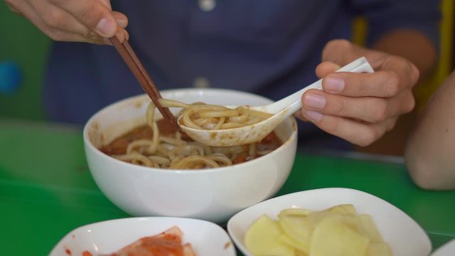Young man in a korean restaurant eats traditional korean noodle Udon