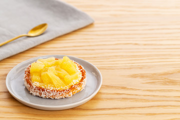 Pineapple tart or tartlet with grated coconut over grey napkin with a golden spoon on a wooden background with copy space.