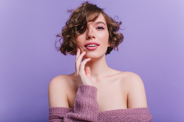 Close-up photo of adorable female model with pink makeup. Studio portrait of shy inspired girl with dark curly hair isolated on purple background.