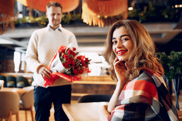 Couple in a restaurant. Lady in a black dress. Man gives flowers to a woman