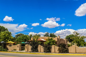 Obraz premium Beautiful stucco mud southwestern USA house with fence and landscaping and umbrellas beside road with curb painted yellow under very blue sky with puffy clouds