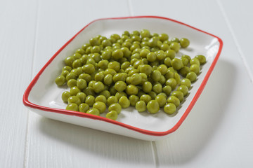 Canned green peas in a white plate with a red border.