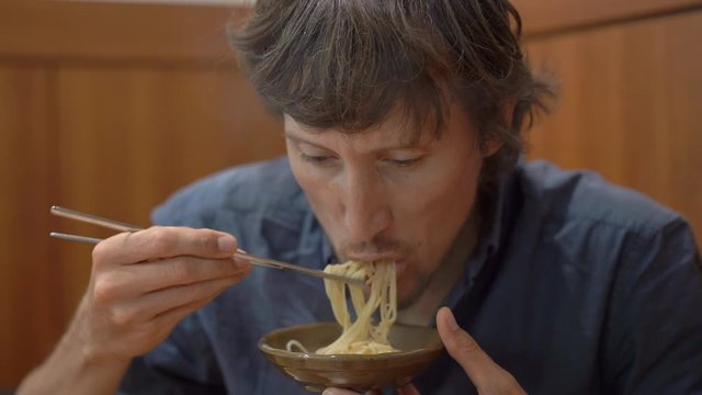 Young man in a korean restaurant eats traditional korean noodle Udon