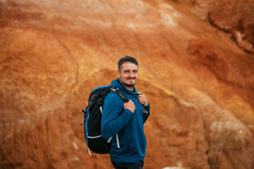 A young male tourist with a backpack stands on top of a mountain. Red mountains in the Altai.Close-up portrait. Traveler in the mountains.Outdoor activity.Summer adventure travel.