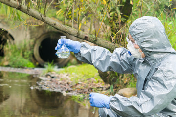 environmental biologist in a protective suit and mask examines water from the river for viruses