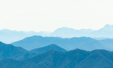 Smokey Valleys high up in the mountain tops, with different shades over each ridge line. Green trees in foreground