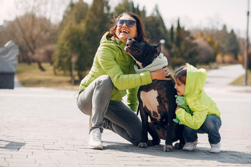 Beautiful mother with daughter. Family in a spring park. Woman in a green jacket. Family with a big dog