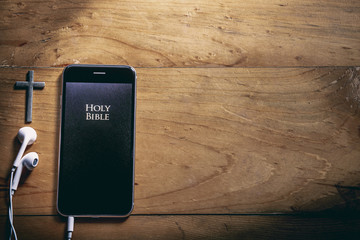 Bible app in smart phones and cross on a wooden table, read and listen to the voice of God concept.
