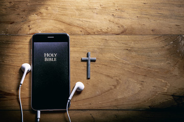 The Bible app in smart phones and silver cross on a wooden table, read and listen to the voice of...