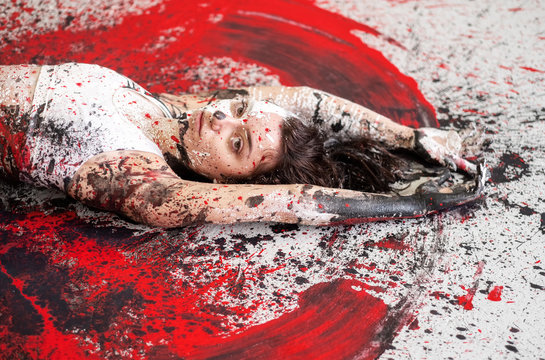Young sexy woman in underwear, sportswear, artistically abstract painted with black, red, white, paint, lies on the floor and spreads the paint on the floor in the form of angel wings.