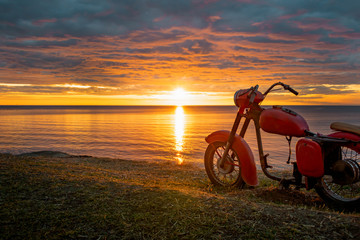 A skeleton of an old red motorcycle against the picturesque sunrise.