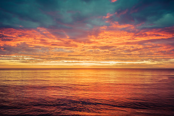 Fototapeta na wymiar Picturesque sunrise over the sea. Dramatic sky colored in orange and red.