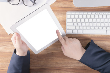 Businessman using tablet over the wooden desk with computer and office supplies in modern work space, pointing finger at blank screen for adding your content. Business and technology concept. Top view