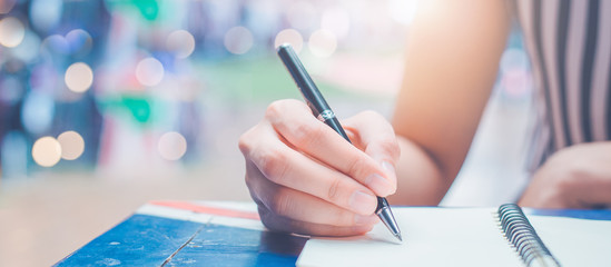 Woman hand is writing on a blank notepad with a pen on a wooden desk.