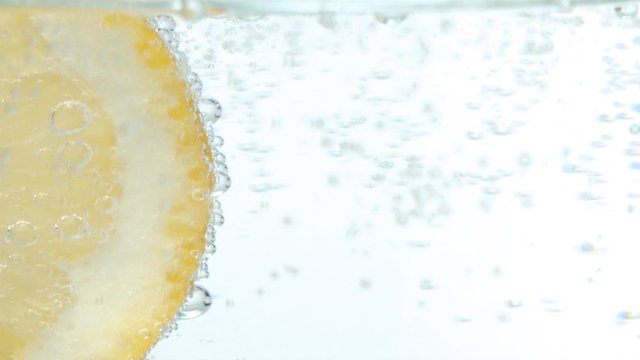 Macro shooting sliced lemon in mineral water on a white background. Naturally carbonated mineral water in a glass. Gas bubbles in slow motion