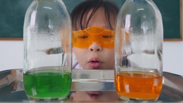 Little asian school girl looking at chemical reaction of liquid in glass bottle.