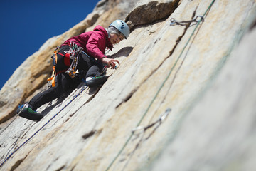 Young woman climber climbs up a vertical rock wall in the mountains, close-up.