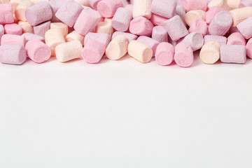 Gentle pink and yellow marshmallows on white paper background with copy space. Sweet food. Selective focus. Pastel color.