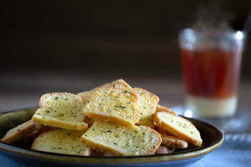 Crispy Breads in black dish and hot tea in glass all put on old wooden table