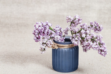 Bouquet of lilac flowers in blue glass vase on blurred background. Rustic style. Selective focus.