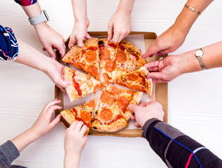 Everyone loves pizza. Close-up top view of young people choosing slices of pizza during lunch indoors.