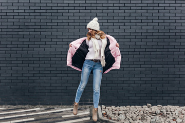 Full-length portrait of slim girl in jeans and pink jacket dancing on the street. Outdoor shot of...