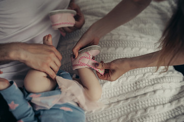 adult hands pull pink shoes on a small child, parental assistance to a small child who can not dress himself