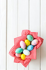 Easter eggs painted in basket on white wooden desk top-down copy space