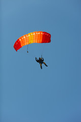 Figure of skydiver under the canopy of a bright red-orange parachute against the blue sky. Parachute jump.