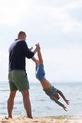 Athletic dad plays with his son on the lake holding his feet above the water