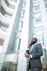 Below view of confident bearded businessman in suit drinking coffee and talking by phone while working on move